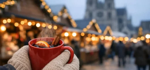 Mains tenant un verre de vin chaud au Marché de Noël d'Amiens, chalets illuminés et cathédrale en fond flou.